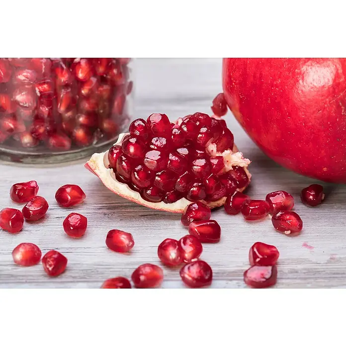 Granado - Punica granatum - Primer plano de semillas de granada frescas y media fruta colocada sobre una mesa con un vaso lleno de semillas al fondo.