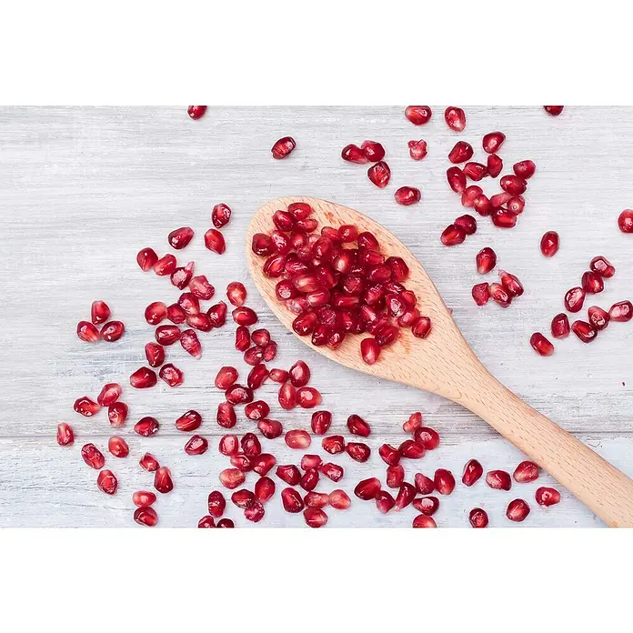 Granado - Punica granatum - Primer plano de semillas de granada en una cuchara de madera, destacando la dulzura y frescura natural de la fruta.\n