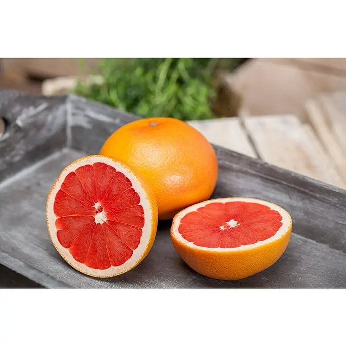 Piardino Árbol frutal Naranjo - Citrus x sinensis, Volumen de la maceta: 10 l - Tres pomelos rojos brillantes, uno entero y dos mitades, dispuestos en una bandeja rústica de madera.