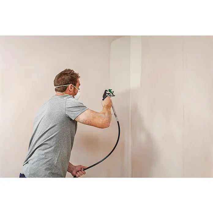 Wagner High Efficiency Airless Sistema de pulverización de pintura Airless Hea 250M - 550 W, Caudal: 1,25 l/min - Un hombre rocía pintura en una pared con un rociador de pintura, logrando un acabado liso y mejorando la apariencia de la habitación.