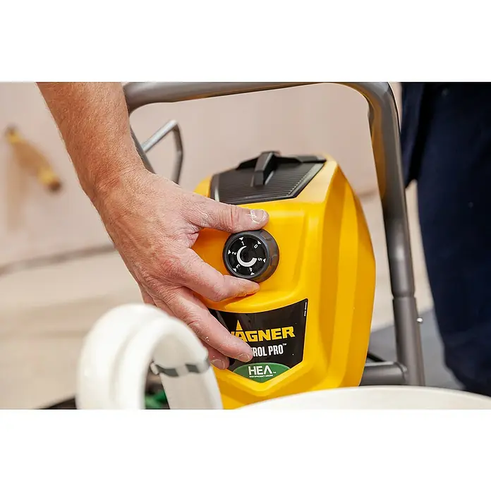 Wagner High Efficiency Airless Farbsprühsystem Control Pro 250 M - 550 W, Förderleistung: 1,25 l/min - Nahaufnahme eines Wagner Control Pro Farbspritzgeräts, das von einer Person bedient wird. Das Gerät ist gelb und hat einen Drehknopf.