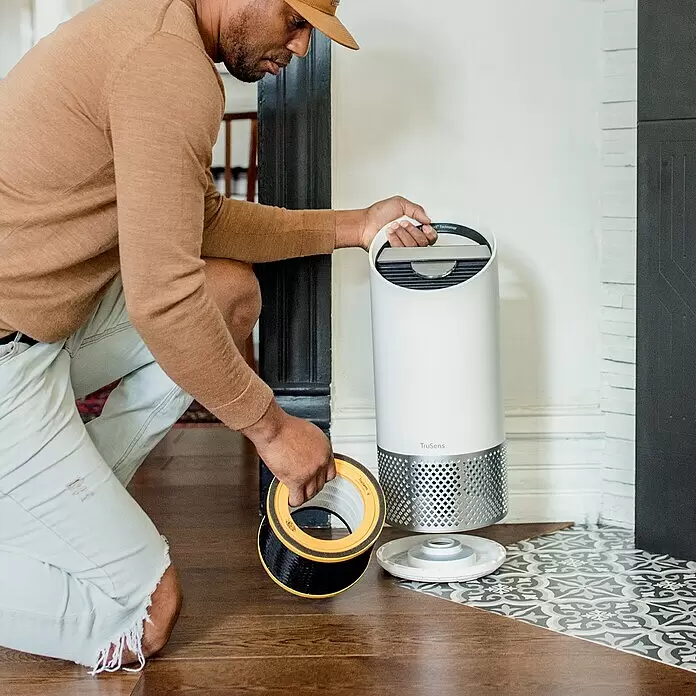 Leitz TruSens HEPA-Filter Gerüche & VOC - Passend für: TruSens Luftreiniger Z-1000 - Mann kniet und wechselt den schwarz-gelben Filter eines weißen TruSens Luftreinigers.