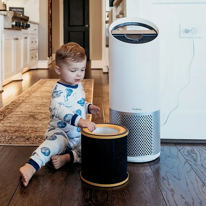 Leitz TruSens HEPA-Filter Gerüche & VOC - Passend für: TruSens Luftreiniger Z-1000 - Ein kleiner Junge sitzt neben einem TruSens Luftreiniger und hält einen Filter. Saubere Luft für die Kleinsten.