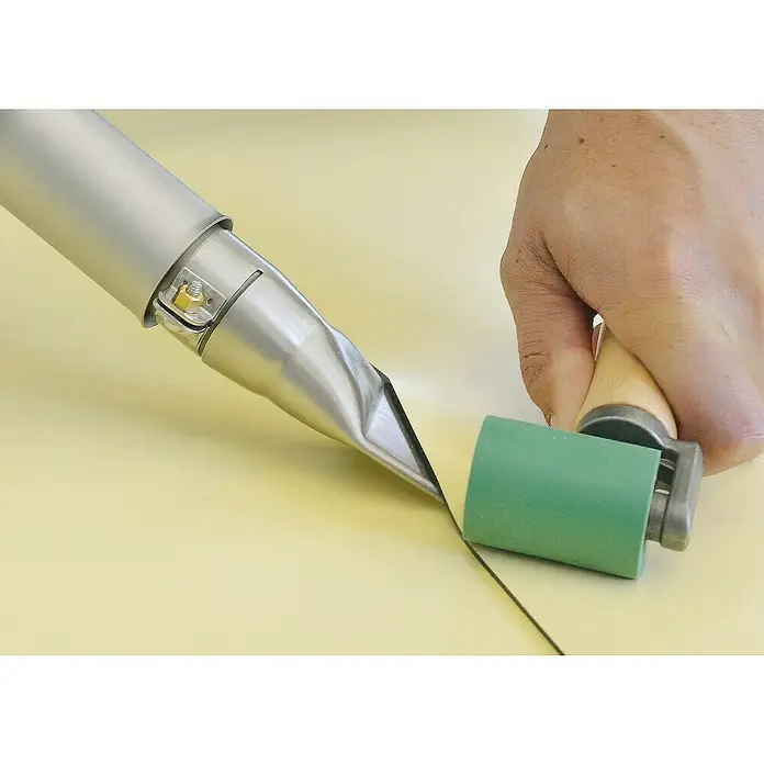 Leister Breitschlitzdüse - Passend für: Heißluftgebläse mit Anschlussdurchmesser Ø 31.5 mm, B x H: 40 x 2 mm - Detailaufnahme eines Föns und einer grünen Andrückrolle auf einer gelben Oberfläche, die zum Verlegen von Böden verwendet werden.