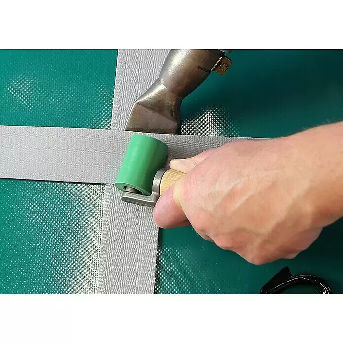 Leister Andruckrolle - Breite: 40 mm - Hand drückt einen grauen Streifen mit einer grünen Andruckrolle, verschweißt ihn mit der Oberfläche.