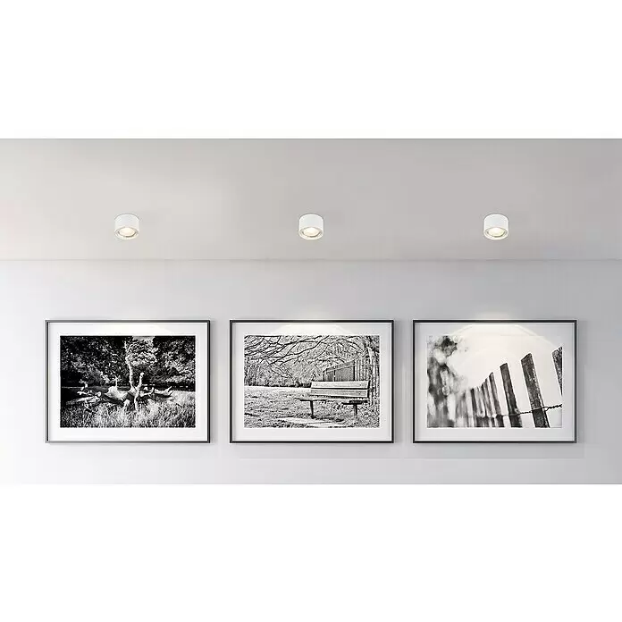 Globo LED-Deckenleuchte rund Serena - 12 W, Ø x H: 113 mm x 8 cm, Weiß, Klar, Warmweiß - Drei weiße zylindrische Deckenstrahler beleuchten gerahmte Schwarz-Weiß-Kunst an einer Wand.