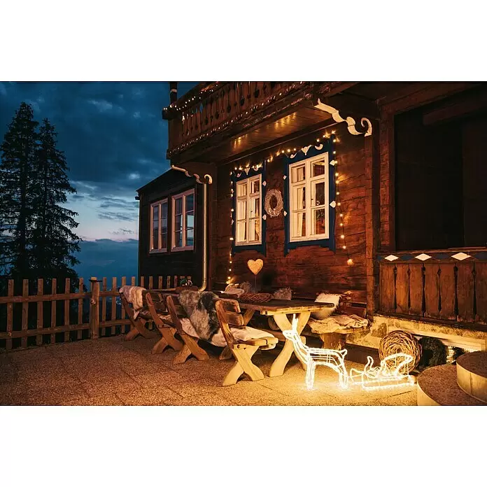 Tween Light LED-Lichtschlauch Rentier mit Schlitten - Anwendungsbereich: Außen, Warmweiß - Beleuchtete Rentier- und Schlittenfiguren auf einer gemütlichen Berghütten-Terrasse, mit Lichterketten dekoriert unter dunklem Himmel.