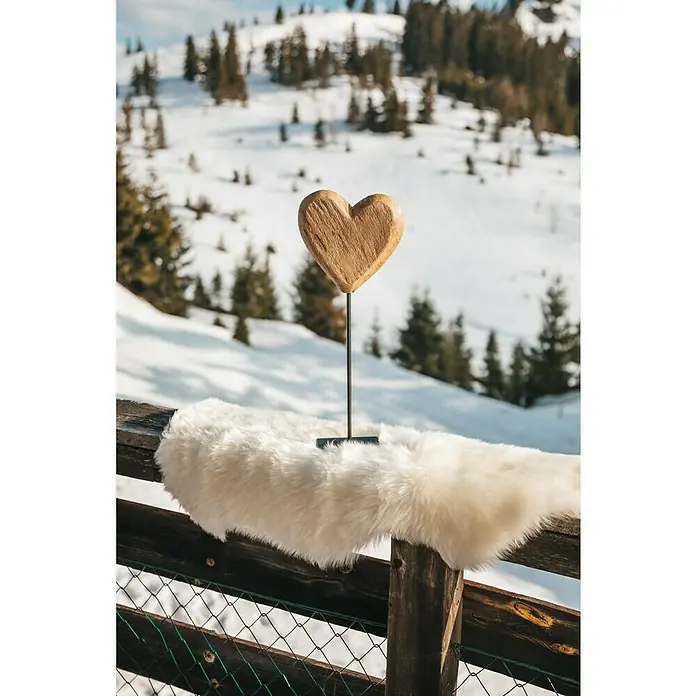 Esbeco Schaffell - Weiß, 80 x 50 cm, 100 % Echtfell - Nahaufnahme eines Holzherzens auf einem Geländer mit einem Fell und einer verschneiten Berglandschaft im Hintergrund.