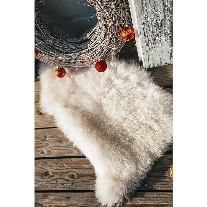 Esbeco Schaffell - Weiß, 80 x 50 cm, 100 % Echtfell - Nahaufnahme eines flauschigen, weißen Teppichs mit Weihnachtskugeln auf einer Holzoberfläche, der eine festliche und gemütliche Atmosphäre schafft.