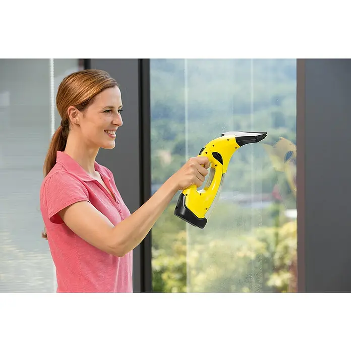 Kärcher Limpiadora de cristales de batería WV2 Plus N - Sin batería, Volumen de recipiente: 0,1 l - Una mujer limpia ventanas con un aspirador de ventanas inalámbrico Kärcher WV amarillo, que garantiza una limpieza sin rayas.