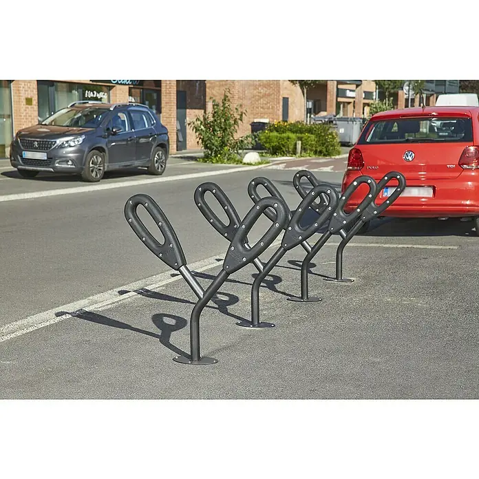 Mottez Fahrradständer - L x B x H: 95 x 16 x 79 cm, 2 Bügel - Fahrradständer aus schwarzem Metall auf Asphalt mit zwei Autos im Hintergrund.