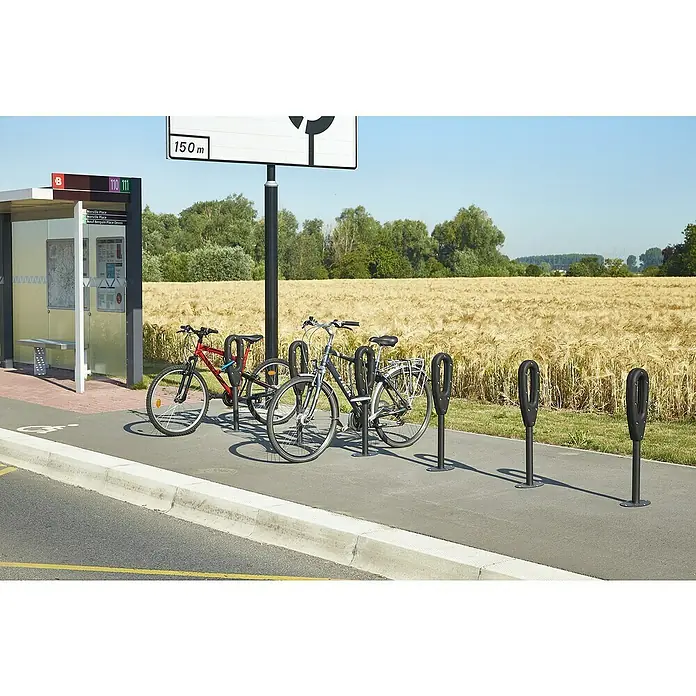 Mottez Fahrradständer - L x B x H: 26 x 16 x 80 cm, 1 Bügel - Fahrradabstellanlage mit mehreren Fahrrädern an einer Haltestelle vor einem Getreidefeld.