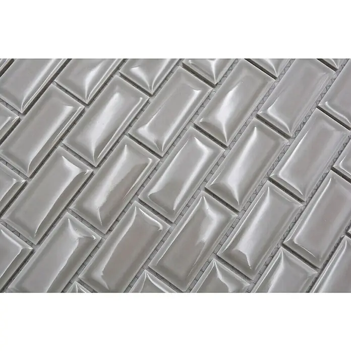 Mosaikfliese Brick Bond Diamond CBC 10230 x 30 cm, Grau, Glänzend - Nahaufnahme von schimmernden, hellgrauen, rechteckigen Fliesen, die in einem Fischgrätmuster angeordnet sind. Die Fliesen haben eine leicht gewölbte Oberfläche.