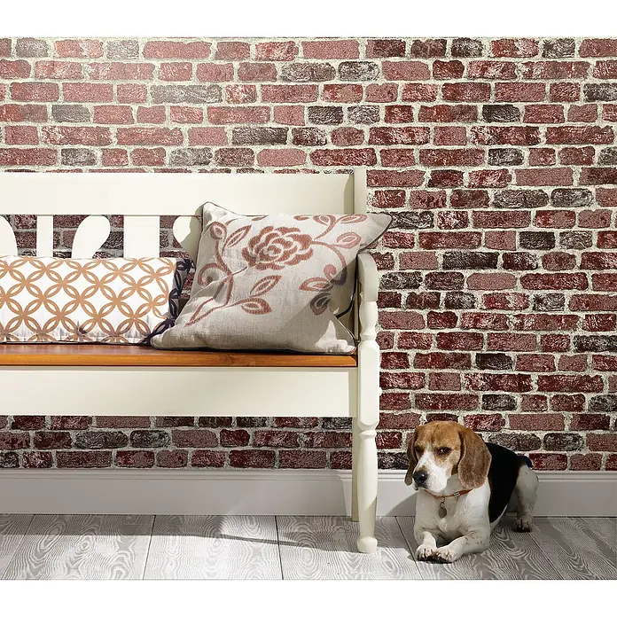 Marburg Sand & Stones Vliestapete Steinmauer II - Rot, Steinoptik, 10,05 x 0,53 m - Einrichtungsszene mit einer Bank, Kissen und einem niedlichen Beagle vor einer roten Backsteinmauer.