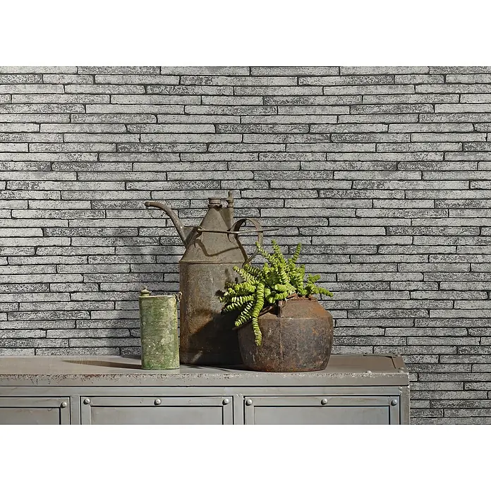 Marburg Sand & Stones Vliestapete Steinmauer I - Mittelgrau, Steinoptik, 10,05 x 0,53 m - Antike Dekoration mit einer Grünpflanze, einer alten Ölkanne und einer grünen Dose auf einer grauen Kommode vor einer grauen Ziegelwand.