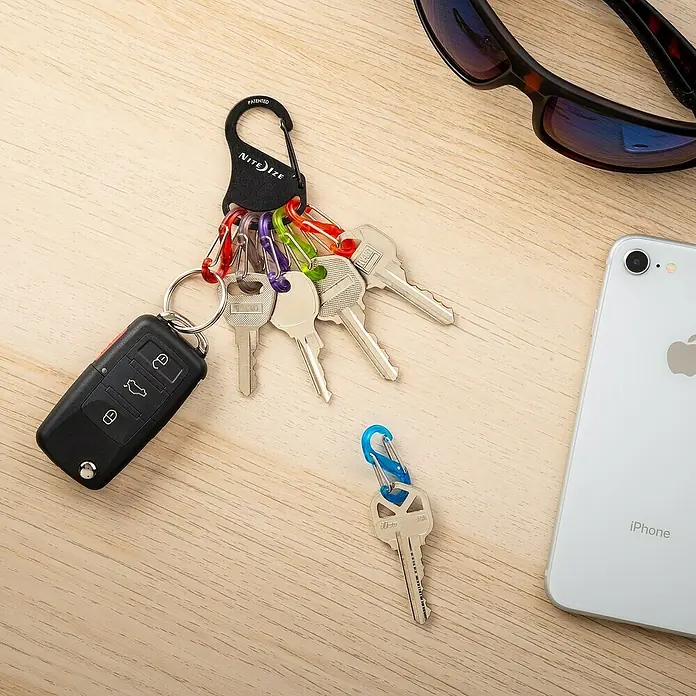Nite Ize Mosquetón KeyRack - L x An: 12 x 2 mm - Llavero con mosquetón Nite Ize, varias llaves, una llave de coche y una llave separada sobre una mesa de madera.