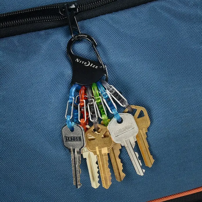 Nite Ize Mosquetón KeyRack - L x An: 12 x 2 mm, Acero inoxidable - Llavero con varias llaves unidas a un mosquetón Nite Ize, colgando de una bolsa azul.