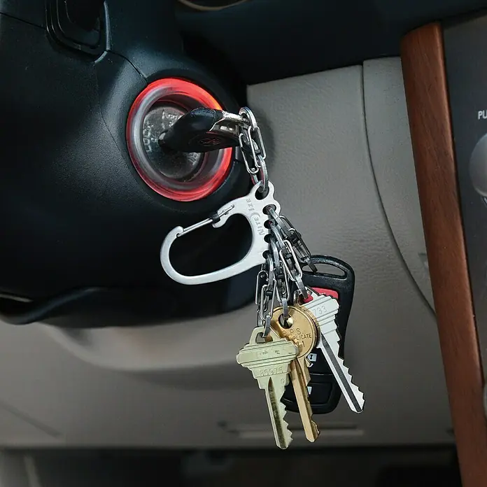 Nite Ize Karabinerhaken BigFoot Locker KeyRack - L x B: 140 x 20 mm, Edelstahl - Nahaufnahme von einem Schlüsselbund mit verschiedenen Schlüsseln, die an einem Nite Ize-Karabiner befestigt sind, im Zündschloss eines Autos.