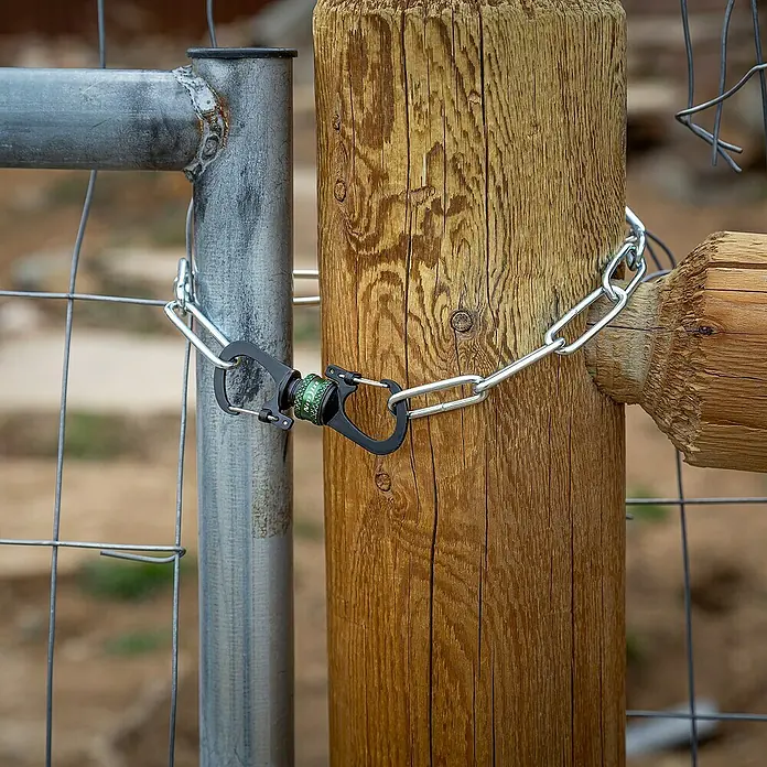 Nite Ize Doppelkarabiner Slidelock 360° Magnetic Lock - L x B: 19 x 2,05 cm, Aluminium, Anthrazit - Nahaufnahme eines Torriegels mit Kette und Karabinerhaken, der ein Holztor sichert.