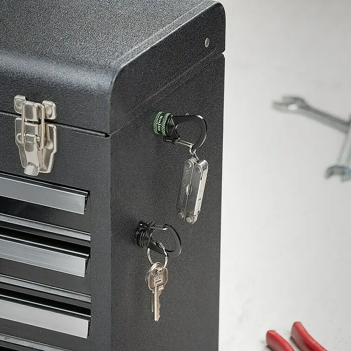 Nite Ize Doppelkarabiner Slidelock 360° Magnetic Lock - L x B: 19 x 2,05 cm, Aluminium, Anthrazit - Nahaufnahme einer schwarzen Werkzeugkiste mit angebrachten Schlüsselanhängern und Werkzeugen, die auf einer weißen Oberfläche liegen.