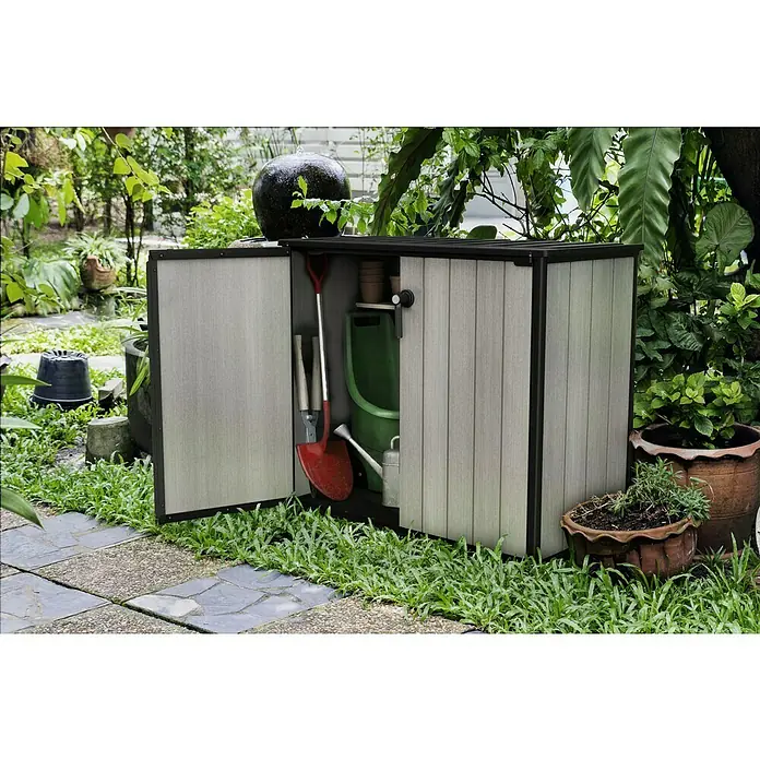 Keter Truhe Patio Store - L x B x H: 73,6 x 140 x 120 cm, Grau - Garten Aufbewahrungsschrank mit geöffneter Tür, gefüllt mit Gartengeräten wie einer Schaufel und einer Gießkanne.