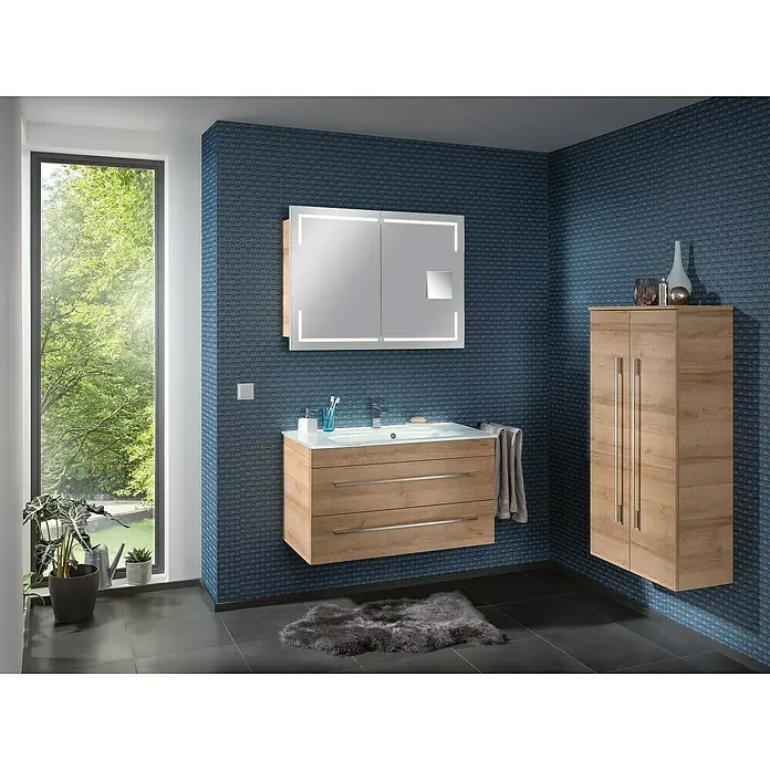 Camargue Stella Waschtischunterschrank - 99,4 x 48,8 x 55 cm, Mit Beleuchtung, Berg Eiche - Elegantes Badezimmer mit Waschtischunterschrank in Holzoptik, beleuchtetem Spiegelschrank und passendem Hochschrank an einer blau gefliesten Wand.