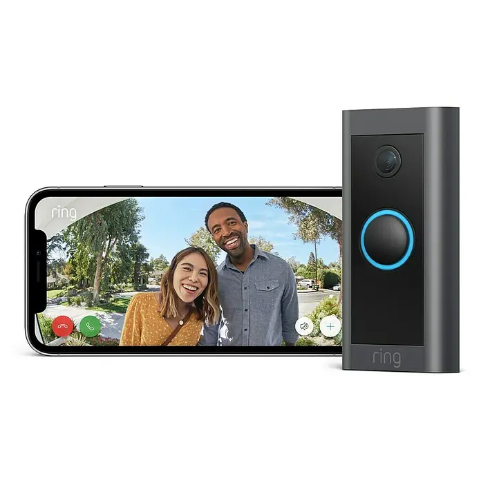 Ring Türklingel mit Kamera Video Doorbell Wired - Bronze, 1.920 x 1.080 Pixel (Full HD), 2,24 x 4,57 x 10,1 cm, Smarte Steuerung: Ring App - Das Bild zeigt eine Ring-Videotürklingel neben einem Smartphone, das eine Live-Ansicht von zwei Personen vor einer Haustür anzeigt.
