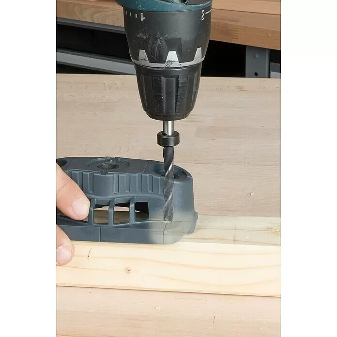 Wolfcraft Bohrhilfe - Lochdurchmesser: 35 mm - 12 mm - Eine Hand hält eine graue Bohrschablone auf einem hellen Holzbrett, während ein Akkubohrer mit Metallbohrer in das Holz bohrt.
