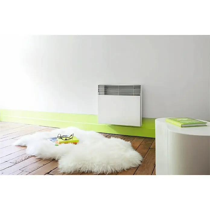 Bruguer Esmalte para radiador - Blanco, Satinado, 750 ml - Un radiador blanco en una pared blanca, con una alfombra de piel de oveja, gafas y libros debajo. Un libro verde está sobre una mesa redonda.