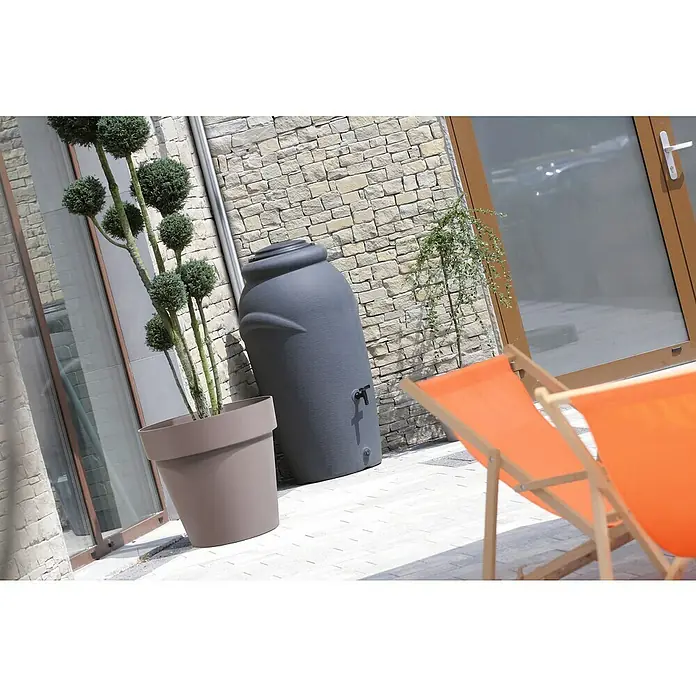 Regenspeicher Aquacan Baby - 210 l, Grau - Ein grauer Regenspeicher steht neben einem bepflanzten Topf auf einer Terrasse. Der Regenspeicher hat einen kleinen Wasserhahn.