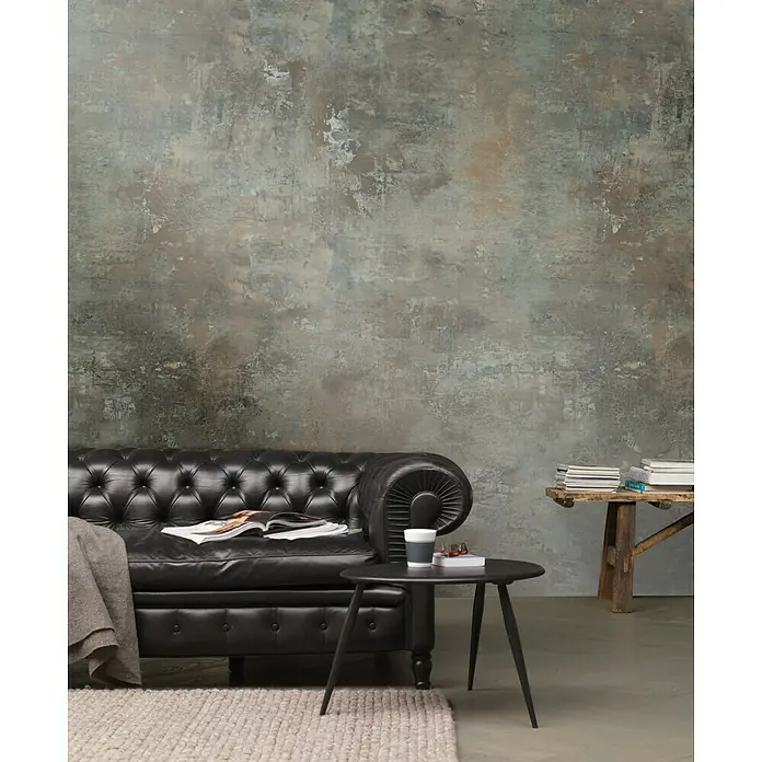 Rasch Factory 4 Fototapete Digitaldruck - 212 x 300 cm, Kupfer - Ein Interieur mit einem Chesterfield-Sofa, einem kleinen Tisch und einem Bücherstapel vor einer strukturierten Wand.