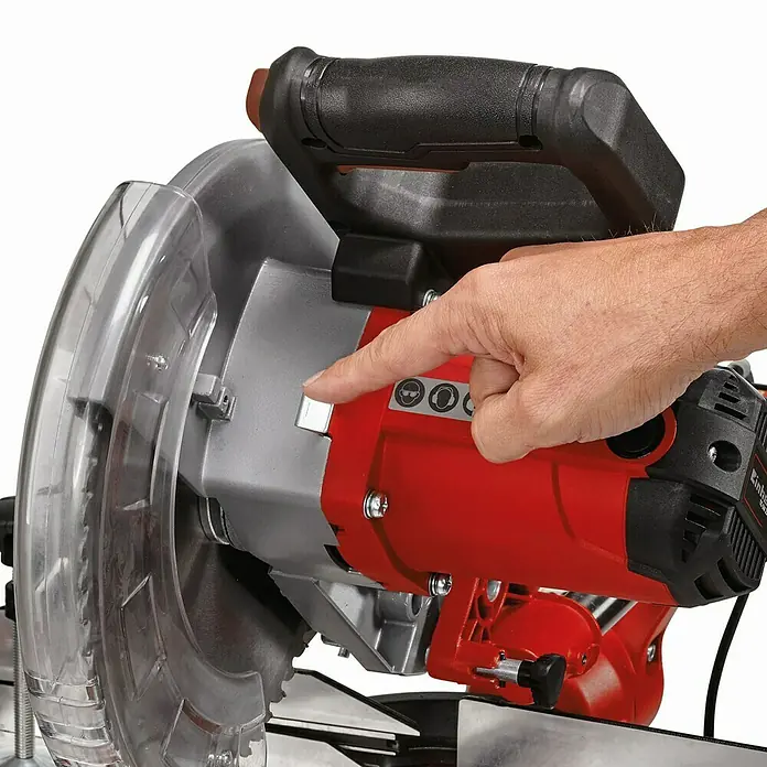 Einhell Sierra ingletadora telescópica TC-SM 2531/2 U - 1.900 W, Diámetro hoja de sierra: 254 mm, Número de revoluciones de marcha en vacío: 1.900 r.p.m. - Un operador presiona el botón de una sierra ingletadora Einhell roja y plateada, que cuenta con una protección transparente.