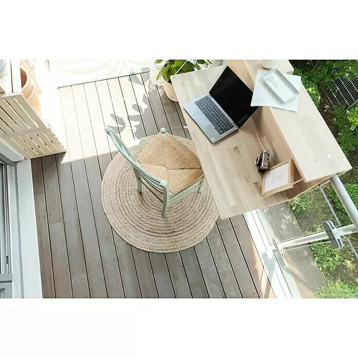 Juteteppich Jute - Natur, Durchmesser: 100 cm, 100% Jute - Hellgrüner Stuhl mit geflochtener Sitzfläche, runder Juteteppich und Holztisch mit Laptop auf einem Balkon.