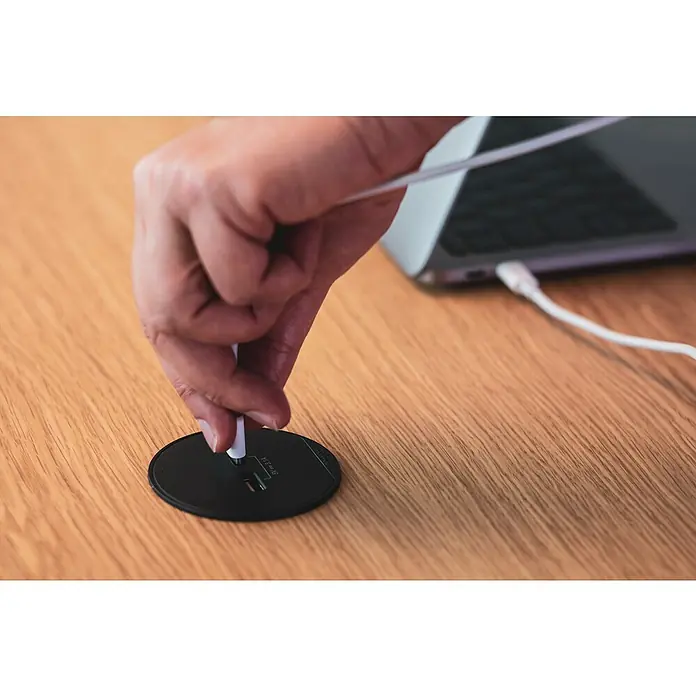 Schneider Electric Cargador inalámbrico - Negro/Verde - Un elegante concentrador USB negro redondo sobre un escritorio de madera que se está conectando, con un portátil al fondo.