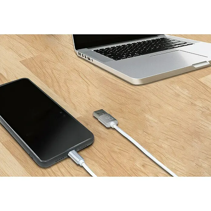 BAUHAUS USB-Ladekabel - Weiß, 1 m, USB A-Stecker, Lightning-Stecker - Weißes USB-Kabel zum Aufladen eines Smartphones auf einem Tisch neben einem Laptop.