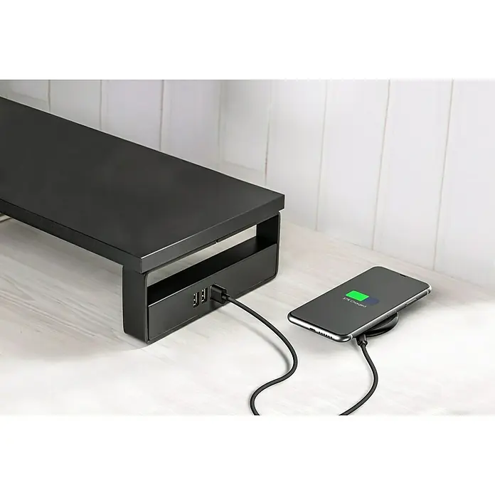 Voltomat Monitor-Erhöhung - Schwarz - Ein schwarzer Monitorständer mit USB-Anschlüssen und ein Handy, das drahtlos geladen wird, stehen auf einem weißen Tisch.