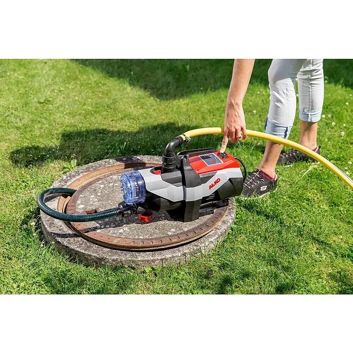 AL-KO Easy Gartenpumpe Jet 3600 Easy - 850 W, 3.600 l/h, 3,8 bar - Eine AL-KO Jet-Wasserpumpe auf einem Betonschachtdeckel mit einer Person, die den Netzschalter betätigt, um die Pumpe zu starten.