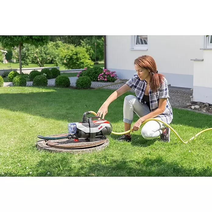 AL-KO Easy Gartenpumpe Jet 3600 Easy - 850 W, 3.600 l/h, 3,8 bar - Eine Frau schließt eine grau-rote AL-KO Gartenpumpe mit transparentem Filter an einen Schlauch an, neben einem Kanaldeckel.