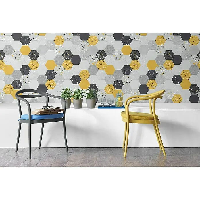 Grosfillex Panel de pared Element 3D Tom Jaune - L x An: 260 x 37,5 cm, Gris/Negro/Amarillo - La imagen muestra una decoración de pared elegante con baldosas hexagonales en amarillo, gris y patrones de terrazo, complementada con sillas modernas y plantas.