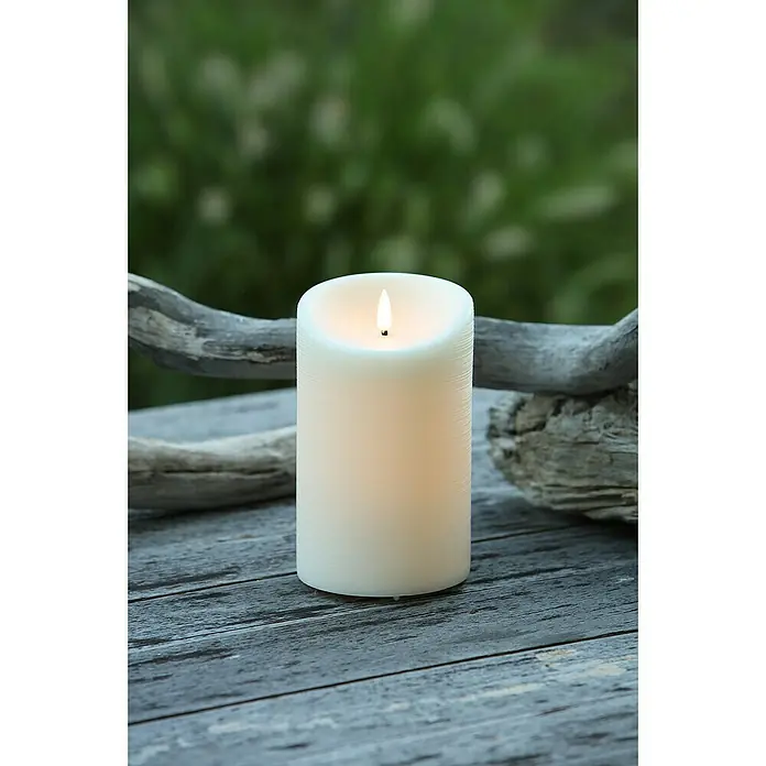 Vela LED para exteriores Elephant - Ø x Al: 10 x 16 cm, Crema, Cera natural - Primer plano de una vela LED blanca con simulación de llama sobre una superficie de madera gris, creando un ambiente acogedor.