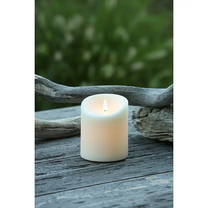 Vela LED para exteriores Elephant - Ø x Al: 10 x 12 cm, Crema, Cera natural - Primer plano de una vela LED blanca sin llama sobre una mesa de madera erosionada con ramas al fondo.
