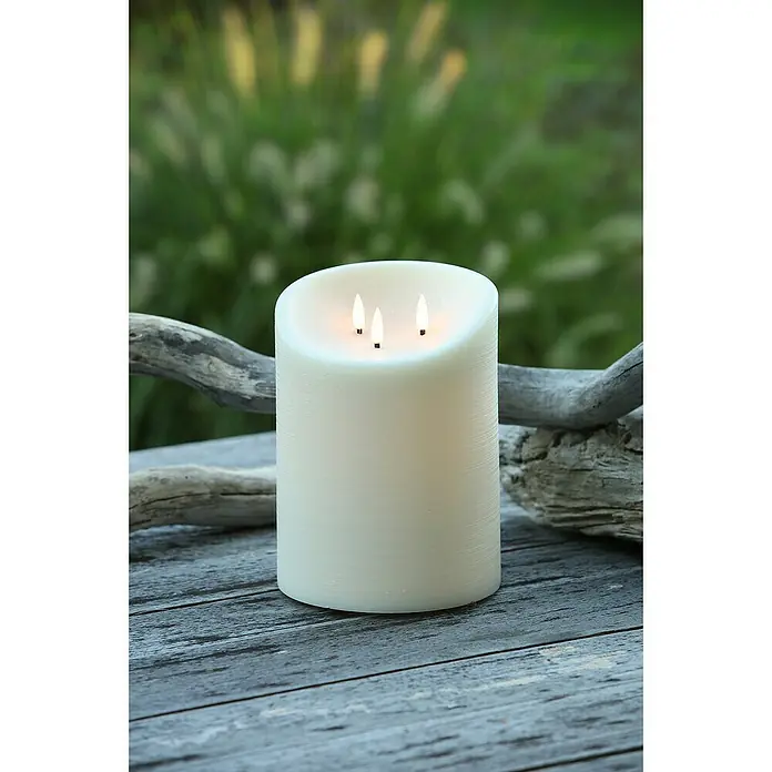 LED-Outdoor-Kerze Elephant - Ø x H: 15 x 20 cm, Creme, Echtwachs - Nahaufnahme einer elfenbeinfarbenen Stumpenkerze mit drei Dochten auf einer grauen Holzoberfläche vor einem grünen Hintergrund.