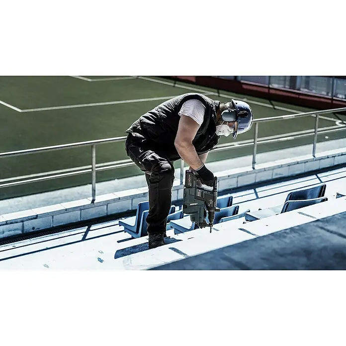 Bosch Expert Broca para hormigón y mampostería -7X - 1 ud., Diámetro de la broca: 5 mm, 100 mm - Un trabajador de la construcción usa un taladro percutor Bosch para hacer agujeros en una superficie de hormigón. Lleva equipo de protección por seguridad.