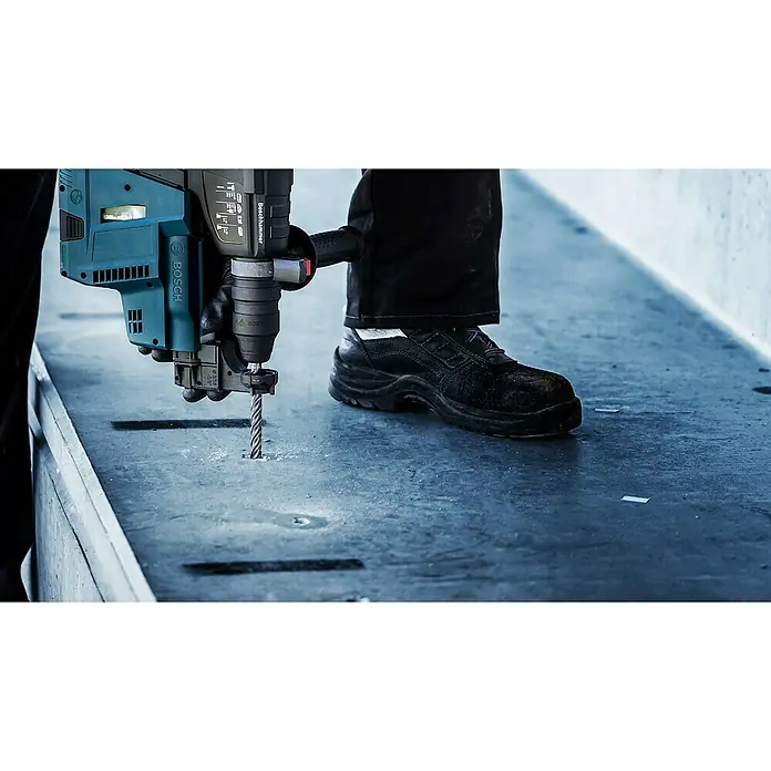 Bosch Expert Beton- & Steinbohrer SDS Plus-7X - 1 Stk., Durchmesser Bohrer: 8 mm, 200 mm - Der Boschhammer bohrt ein Loch in eine Betonplatte. Das Werkzeug ist blau und schwarz, während der Arbeiter Sicherheitsschuhe und Handschuhe trägt.