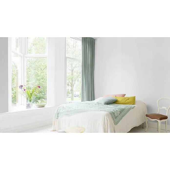 Rasch Vliestapete Feel Good Glasfaser-Optik - Weiß, Uni, 10,05 x 0,53 m, Wabenstruktur - Ein helles Schlafzimmer mit einem gemütlichen Bett, dekoriert mit farbenfrohen Kissen und einer leichten Decke, neben einem Fenster.