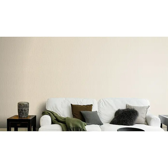 Rasch Kimono Vliestapete Muster - Beige, Uni, 10,05 x 0,53 m - Beige Vliestapete mit feiner Textur über einer weißen Couch mit Kissen und einer grünen Decke, die für ein gemütliches Ambiente sorgt.