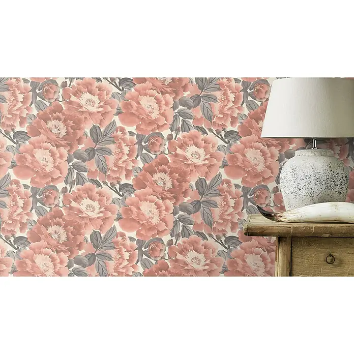 Rasch Kimono Vliestapete Blumen - Rosa, Floral, 10,05 x 0,53 m - Detailaufnahme einer Wand mit floral gemusterter Tapete in zarten Rosatönen und grauen Blättern, neben einer Tischlampe.