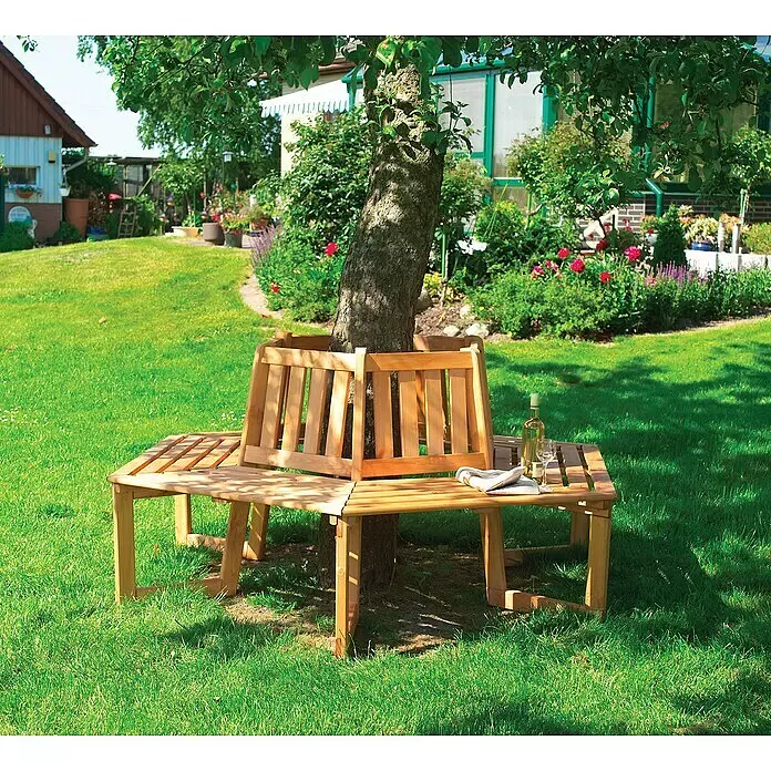 Promadino Baumbank 360° - Kiefer, Honigbraun, Ohne Auflage - Helle hölzerne Baumbank mit Lattenrosten und Rückenlehnen, die einen Baum in einem sonnigen Garten umgibt. Eine Weinflasche und ein Glas stehen darauf.