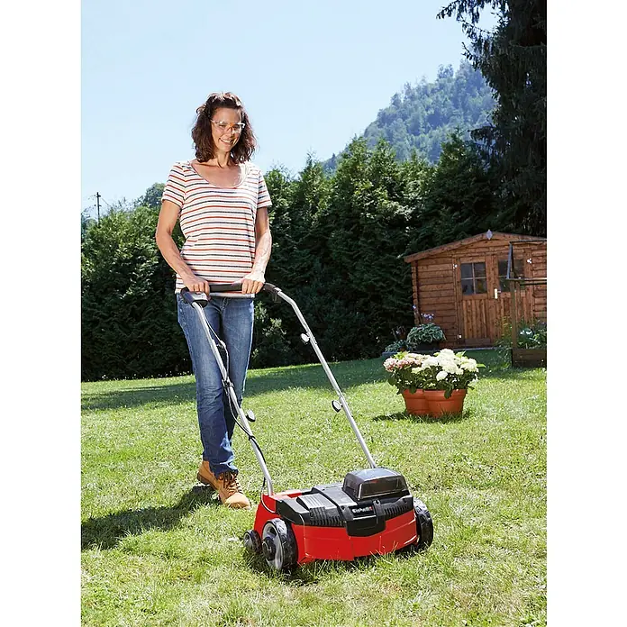 Einhell PXC 18V Escarificador de batería GC-SC 36/31 Li-Solo - Número de baterías: Sin batería, 18 V, Anchura de trabajo: 31 cm - Mujer usa un aireador de césped en el jardín.