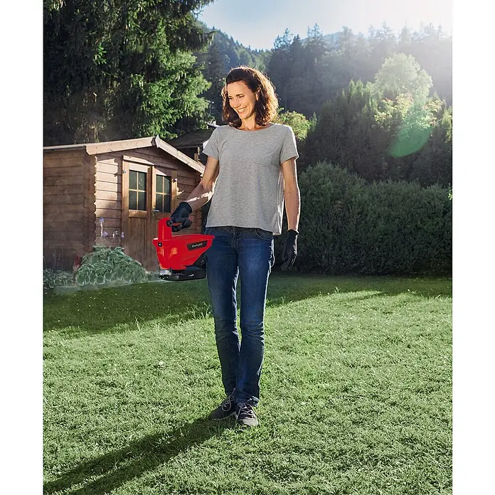 Einhell Power X-Change 18V Handstreuer GE-US 18 Li-Solo - Streubreite: 5 m, Fassungsvermögen: 3,3 l - Frau mit einem Einhell Grassamenstreuer im Garten, bereit, den Rasen zu pflegen.